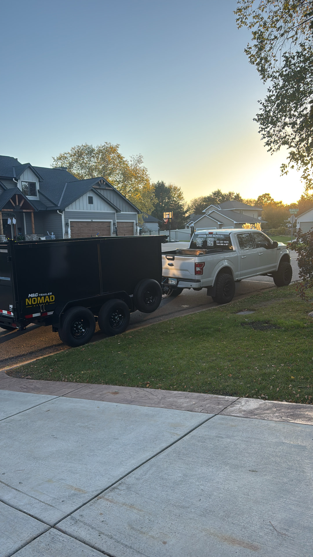 Judson's silver pickup truck and black dump trailer outside a customer's home